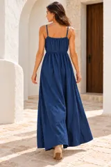 Vestido largo de denim azul oscuro, estilo solera con tirantes finos, escote en V y cordones con borlas en el centro del pecho. Presenta detalles bordados en hilo dorado en el busto y en la parte inferior de la falda, con diseño en niveles y volados.