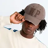 Gorra de estilo desgastado color marrón con letras NP bordadas en el frente y detalles de roturas en la visera.