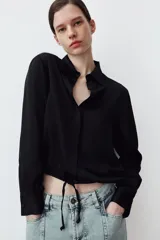 Camisa de satén con cuello solapa, manga larga con puños y bajo ajustable mediante cordones. Presenta cierre frontal con botones ocultos.