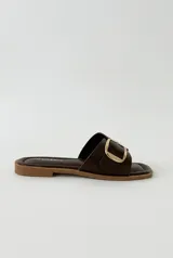 Sandalias Daniel Cassin de símil cuero color marrón oscuro, con una tira ancha cruzada en el empeine y una hebilla metálica rectangular dorada. Presentan puntera cuadrada y suela plana.