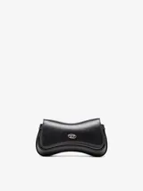 Clutch de cuero bovino negro con diseño curvo inspirado en un control de videojuego. Presenta una solapa frontal con placa metálica plateada con el logo Oval D de la marca y correa regulable desmontable.