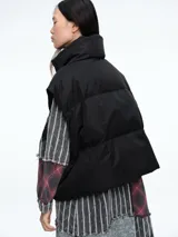 Chaleco puffer de corte holgado y diseño acolchado, con cuello alto, cierre frontal oculto y bolsillos laterales. Ideal para superponer sobre otras prendas.