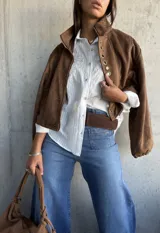 Camisa blanca de corte clásico con sutiles rayas verticales y delicado bordado floral en la parte superior delantera. Presenta cuello camisero, cierre frontal con botones y mangas largas.