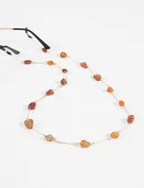 Correa para lentes compuesta por una cadena fina dorada con dijes de piedras de vidrio en tonos naranja y rojizos distribuidos a lo largo de toda la pieza.