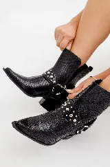 Bota texana corta de cuero negro con textura de piel de serpiente, punta fina y taco cubano. Presenta arnés desmontable con apliques metálicos plateados.
