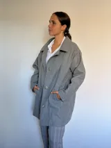 Tapado de paño gris, con cuello solapa, cierre frontal con botones y bolsillos laterales.
