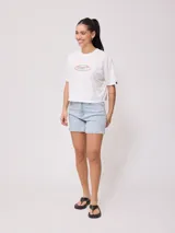 Remera blanca de algodón con calce holgado y largo cropped. Estampado frontal con el logo de la marca Rusty en óvalo con borde rosa y celeste.