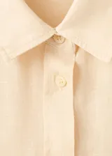 Camisa de lino color beige, de diseño recto con cuello camisero, manga larga con puños abotonados, bolsillo de parche en el pecho y cierre frontal de botones.