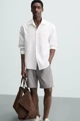 Bermuda negra de corte recto, con cintura elástica ajustable mediante cordón, pliegues frontales y bolsillos de vivo en la espalda. El bajo tiene un dobladillo vuelto.