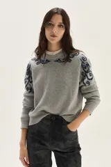 Sweater de tejido de punto gris con cuello redondo, manga larga y diseño de arabescos bordados en azul oscuro sobre los hombros y el pecho.