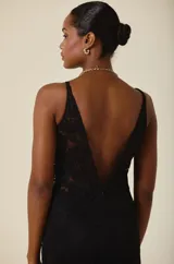 Vestido largo de encaje negro con escote en V y breteles anchos. Presenta un diseño ajustado en el torso que cae con fluidez hacia el ruedo, con una transparencia característica del tejido.