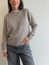 Sweater de tejido suave en color beige con detalle de contraste en blanco en el cuello y los puños. Presenta mangas largas con costura raglán y un ajuste cómodo y versátil.