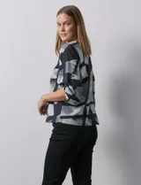 Blusa de gasa con estampado geométrico en tonos negro, gris y celeste. Tiene cuello redondo y mangas 3/4 amplias con abertura y botón.