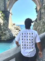 Remera blanca de algodón con cuello redondo y estampado en la espalda con imágenes de cogollos de marihuana y texto "BROKERS HIGH QUALITY GOODS".