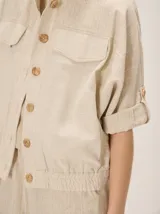 Chaquetas de lino bicolor en tonos blanco y beige, con diseño holgado, cuello alto, cierre frontal de botones, bolsillos con solapa en el pecho y mangas cortas con presilla y botón.