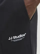 Bermuda deportiva negra de calce relajado, con cintura elástica ajustable mediante cordón, bolsillos laterales y costuras frontales en relieve. Presenta un pequeño estampado de texto en la pierna izquierda.