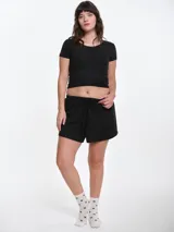 Remera de manga corta entallada en tejido pointelle, con escote redondo y detalle de picot con lazo pequeño en el centro. Diseño ajustado al cuerpo con textura acanalada.