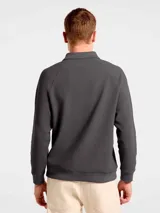 Buzo de manga larga confeccionado en tejido interlock, con cuello tipo polo y cierre frontal de dos botones. Presenta un diseño de corte clásico con puños y ruedo acanalados.