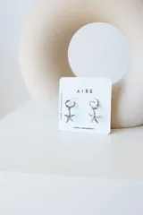 Aros tipo argolla pequeña con dije colgante en forma de estrella de mar, elaborados en acero quirúrgico.