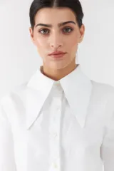 Camisa blanca de lino con mangas largas, cuello camisero grande en punta y cierre frontal con botones.