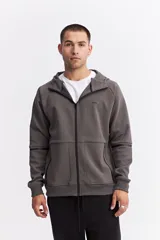 Campera con capucha y cierre frontal, color beige, con detalles de costuras y cierres en negro. Presenta mangas largas con puños acanalados y logo pequeño en el pecho.