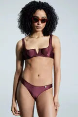 Bombacha de bikini tipo vedetina con acabado metalizado y corte en V en la parte superior delantera. Presenta un aplique metálico decorativo en la cadera.