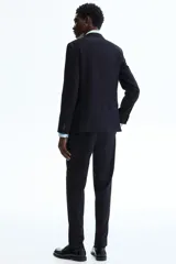 Pantalón de traje negro de corte slim fit, con bolsillos laterales, bolsillos traseros ribeteados y raya marcada en las perneras. Cuenta con cierre de cremallera y corchete oculto.