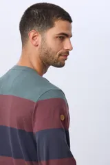 Remera de manga larga con diseño de rayas horizontales en tonos azul marino, beige y verde oscuro. Presenta cuello redondo y una pequeña estampa tipográfica en el pecho, además de una etiqueta decorativa en el ruedo.