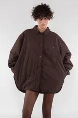 Camisa acolchada marrón con cuello clásico, cierre frontal con botones, manga larga raglán, puños abotonados, bolsillo utilitario en el pecho, bolsillos laterales y canesú abotonado en la espalda.