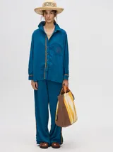 Pantalón de corte holgado y tiro alto con caída recta, color azul petróleo. Presenta una franja lateral decorativa en tonos rojo y amarillo que recorre la pierna, a juego con la camisa de la misma línea.