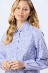 Camisa de manga larga color celeste y blanco, con estampado de motivos botánicos, cuello camisero, cierre frontal con botones y frunces en los puños.
