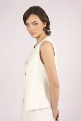 Chaleco blanco sin mangas, con cuello redondo y cierre frontal de botones. El chaleco tiene un corte recto y ligeramente holgado.