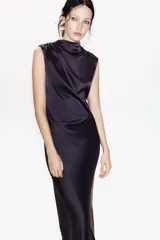 Vestido largo color morado de tejido satinado, sin mangas, con cuello fluido y detalle de drapeado en el lateral.