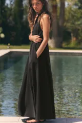 Vestido midi de corte fluido y diseño minimalista, con cuello redondo y mangas sisa. Presenta un cierre en la espalda con abertura y lazada ajustable.