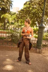 Pantalón cargo de tiro bajo, color marrón rojizo con efecto desgastado u oxidado. Presenta múltiples bolsillos cargo con argollas metálicas en las piernas y cierre frontal con botón claro.