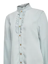 Camisa celeste de denim confeccionada en 100% Tencel, con cuello alto con volado, frente de botones con pequeños volados y puños con volado.