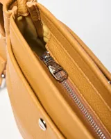 Bandolera de símil cuero color habano, con bolsillo frontal con broche a presión, correa ajustable y logo de la marca en placa metálica.