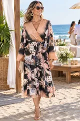 Vestido midi de satén con estampado multicolor en tonos marrón, negro y tostado. Presenta diseño cruzado con escote en V, mangas largas amplias y lazo ajustable en la cintura. La falda incluye un delicado volado en el ruedo.