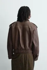 Cazadora biker de corte oversize confeccionada en piel color marrón. Presenta cuello con solapas de pico, cierre frontal asimétrico con cremallera, bolsillos laterales de vivo y bajo con elástico. Las mangas largas cuentan con puños ajustables con cremallera.