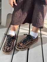 Zapatillas bajas con capellada de cuero y cuero con estampado de leopardo, cordones negros y suela color caramelo.