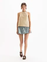 Top Lucille de silueta evasé, calce holgado y corte cropped, confeccionado en poplín Milano de algodón Pima. Cuenta con escote halter de sisa profunda, bretel regulable con ojalillos de níquel que envuelve el cuello, pinzas de entalle y espalda abierta.