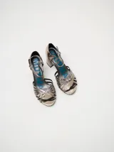 Sandalias de taco alto ancho con diseño retro, confeccionadas en charol negro. Presentan tiras delanteras múltiples entrelazadas, talón cerrado y una correa fina ajustable al tobillo con hebilla metálica.