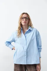 Camisa de corte relajado y diseño clásico, confeccionada en tela de algodón color celeste. Presenta cuello tradicional, cierre frontal con botones y mangas largas con puños rectos.