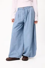 Pantalón de denim estilo palazzo con silueta holgada y diseño de pinzas en la cintura. Presenta un corte amplio y fluido, con cierre frontal y bolsillos laterales.