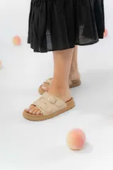 Sandalias color beige con dos tiras anchas con hebillas metálicas doradas, confeccionadas en material gamuzado sintético. Suela acolchada y antideslizante.