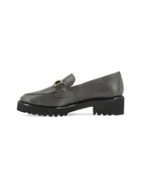 Mocasín de cuero color gris oscuro, con suela track negra de goma y detalle de hebilla metálica dorada en el empeine.