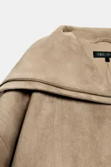 Cazadora bomber marrón de efecto gamuza, con cuello de solapa amplia, manga larga, bolsillos delanteros y cierre frontal asimétrico con cremallera metálica.