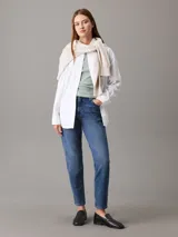 Pantalón de jean azul de corte mom, tiro alto, pierna recta y tobillo ajustado. Confeccionado con denim comfort stretch de peso medio, con un 20% de algodón reciclado. Cuenta con bragueta con cremallera, diseño de cinco bolsillos, herrajes de Calvin Klein e insignia de Piel.