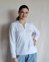 Remera blanca de manga larga con diseño de cuello en V y detalle de tablas frontales. Presenta mangas con sutil frunce en los hombros y puños rectos.