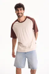 Remera oversize de algodón con diseño raglán, cuerpo en tono crudo y mangas cortas junto con cuello redondo en color marrón.
